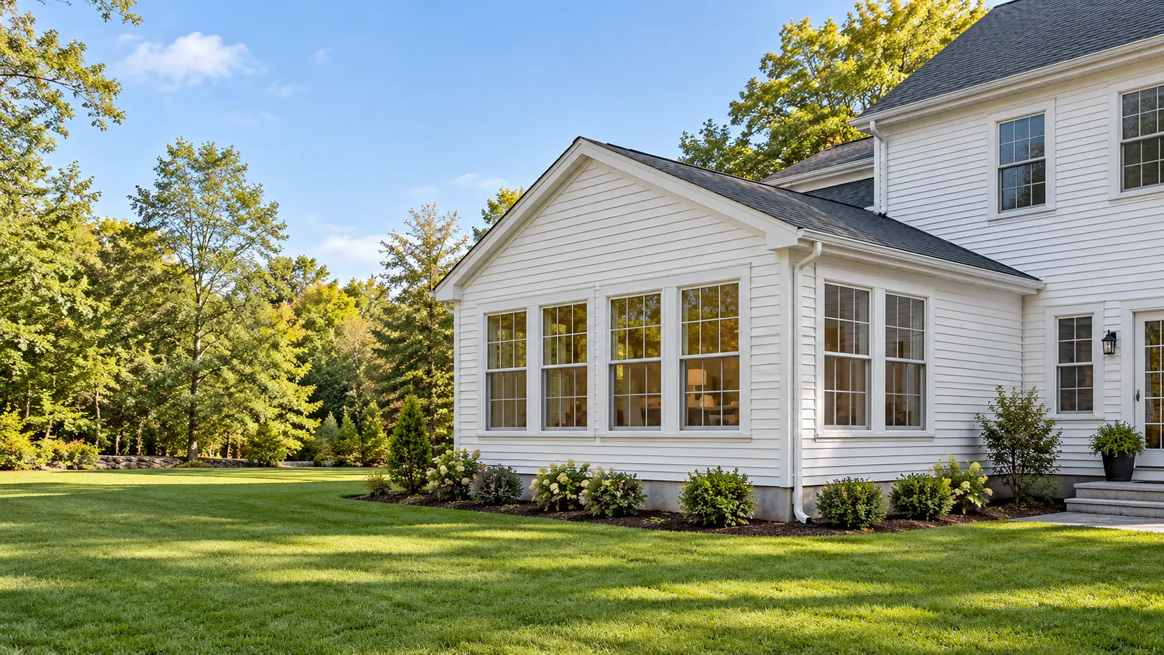 A single-story room addition with a wall of windows on a white New England colonial home.