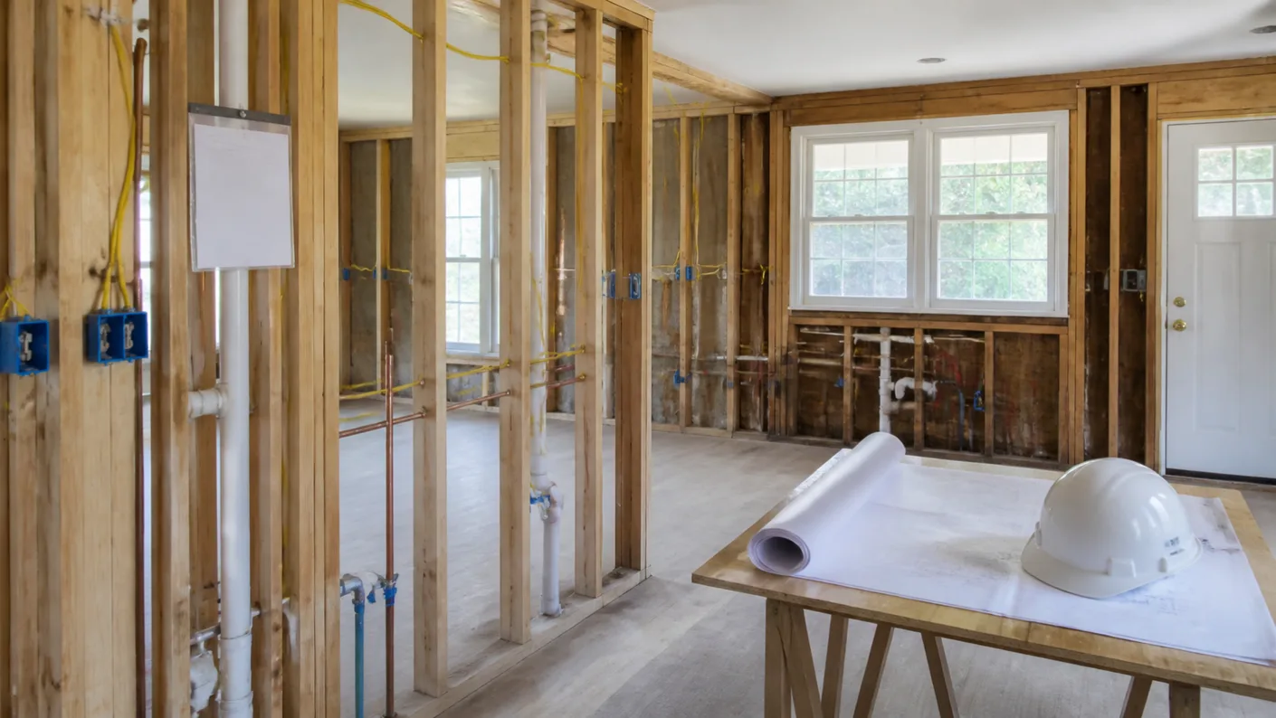 Kitchen remodel permit stage in a Massachusetts home, with open stud walls showing new wiring and plumbing, rolled plans and a hard hat ready for inspection